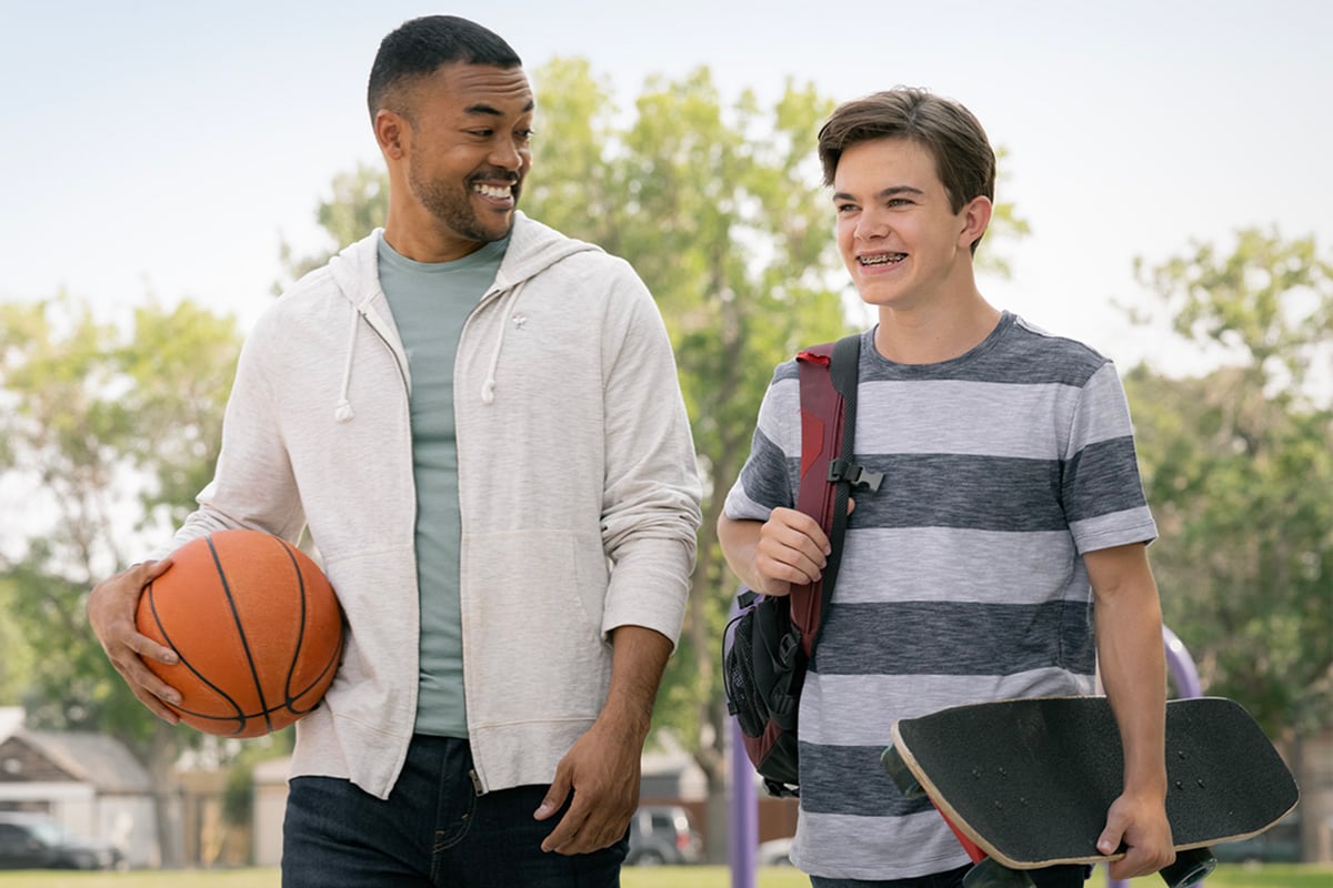 Man with basketball laughs with kid carrying skateboard