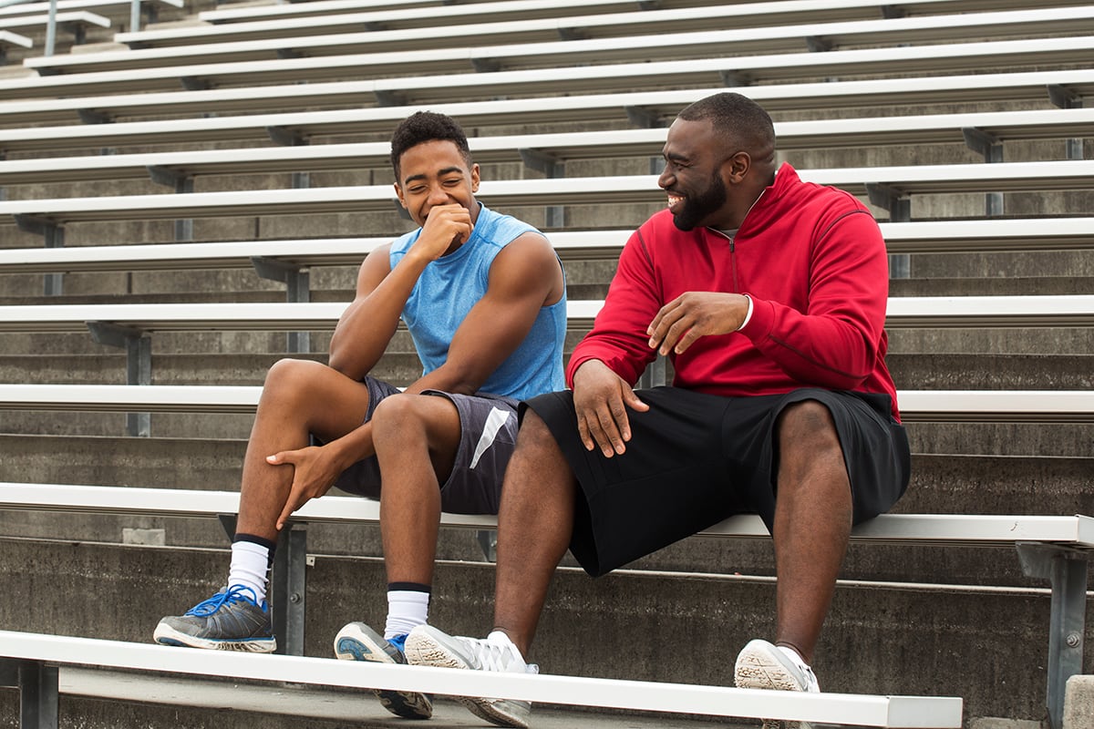 Man and teenager laugh on bleachers