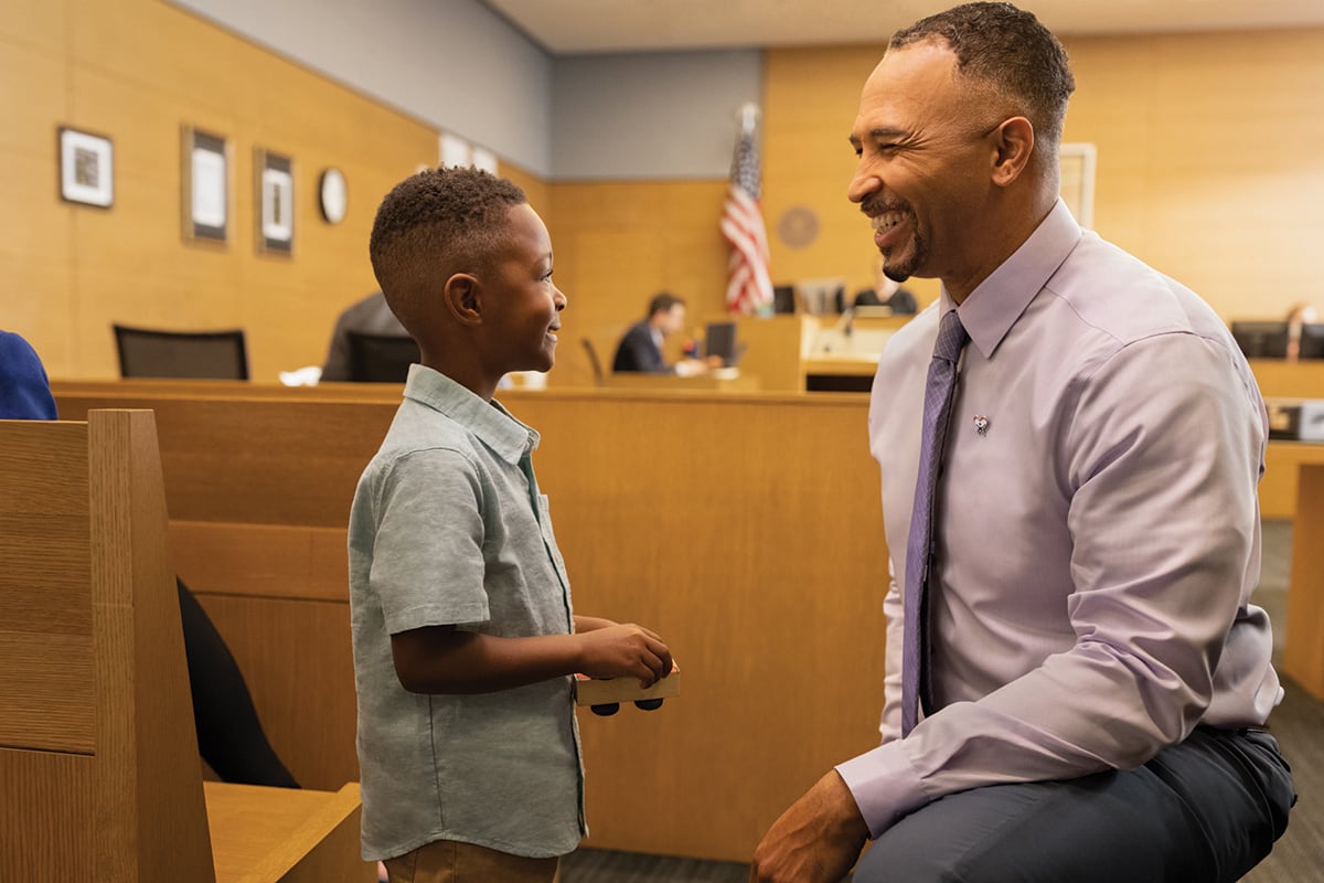 Man in suit smiles with child inside a courtroom